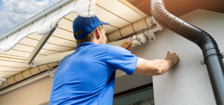 Mann bei der Montage einer Markise an der Hausfassade über dem Balkonfenster
