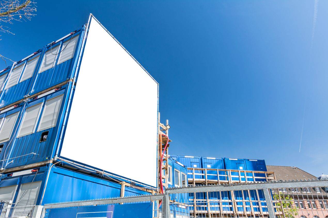 Großflächiges Gerüstbanner auf einem Baucontainer mit blauem Himmel, ideal für Bauwerbung und Unternehmensmarketing.