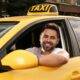 Taxifahrer Jobs: Junger Mann am Steuer eines gelben Taxis, lächelt freundlich aus dem Fenster
