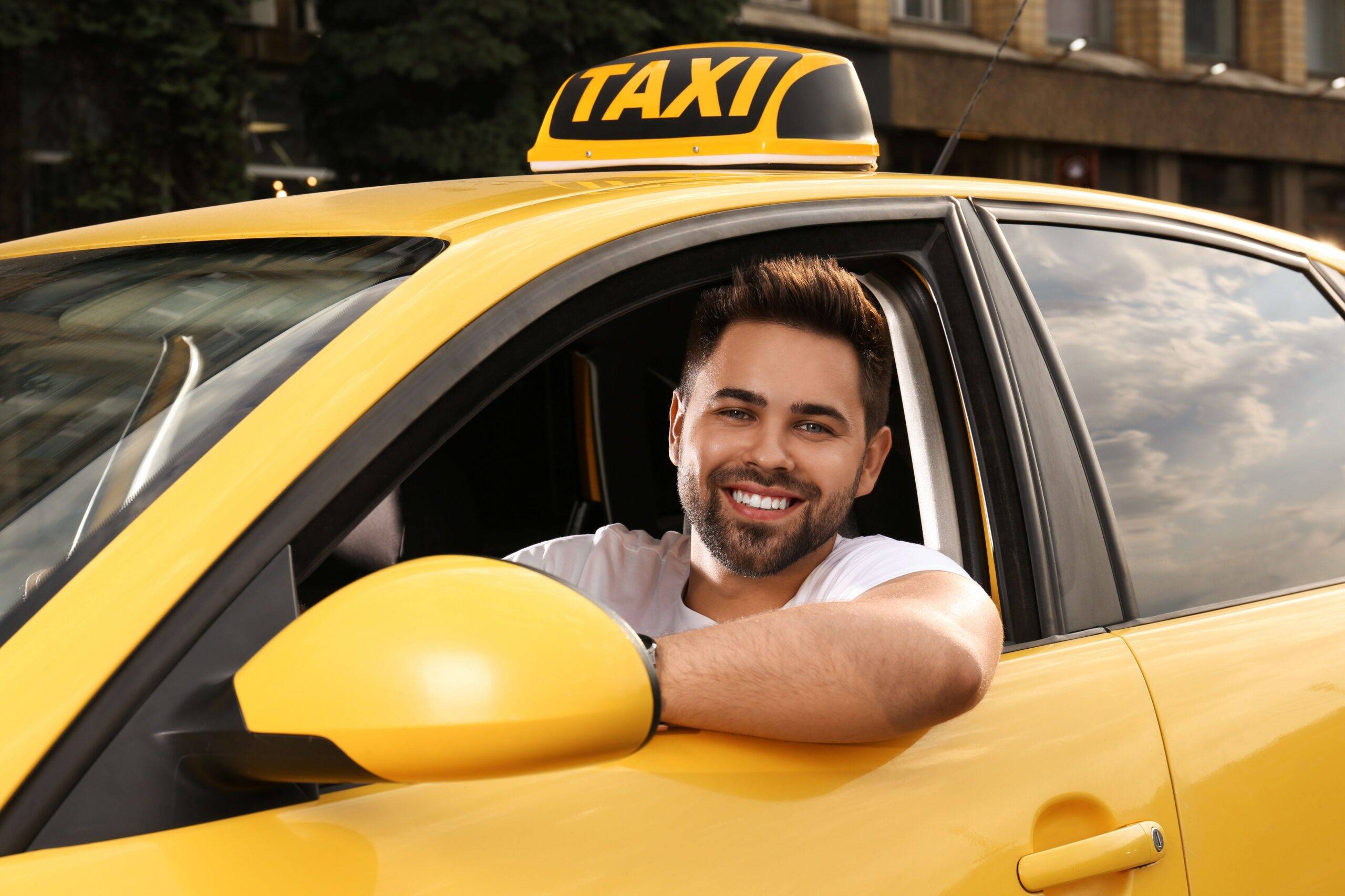 Taxifahrer Jobs: Junger Mann am Steuer eines gelben Taxis, lächelt freundlich aus dem Fenster