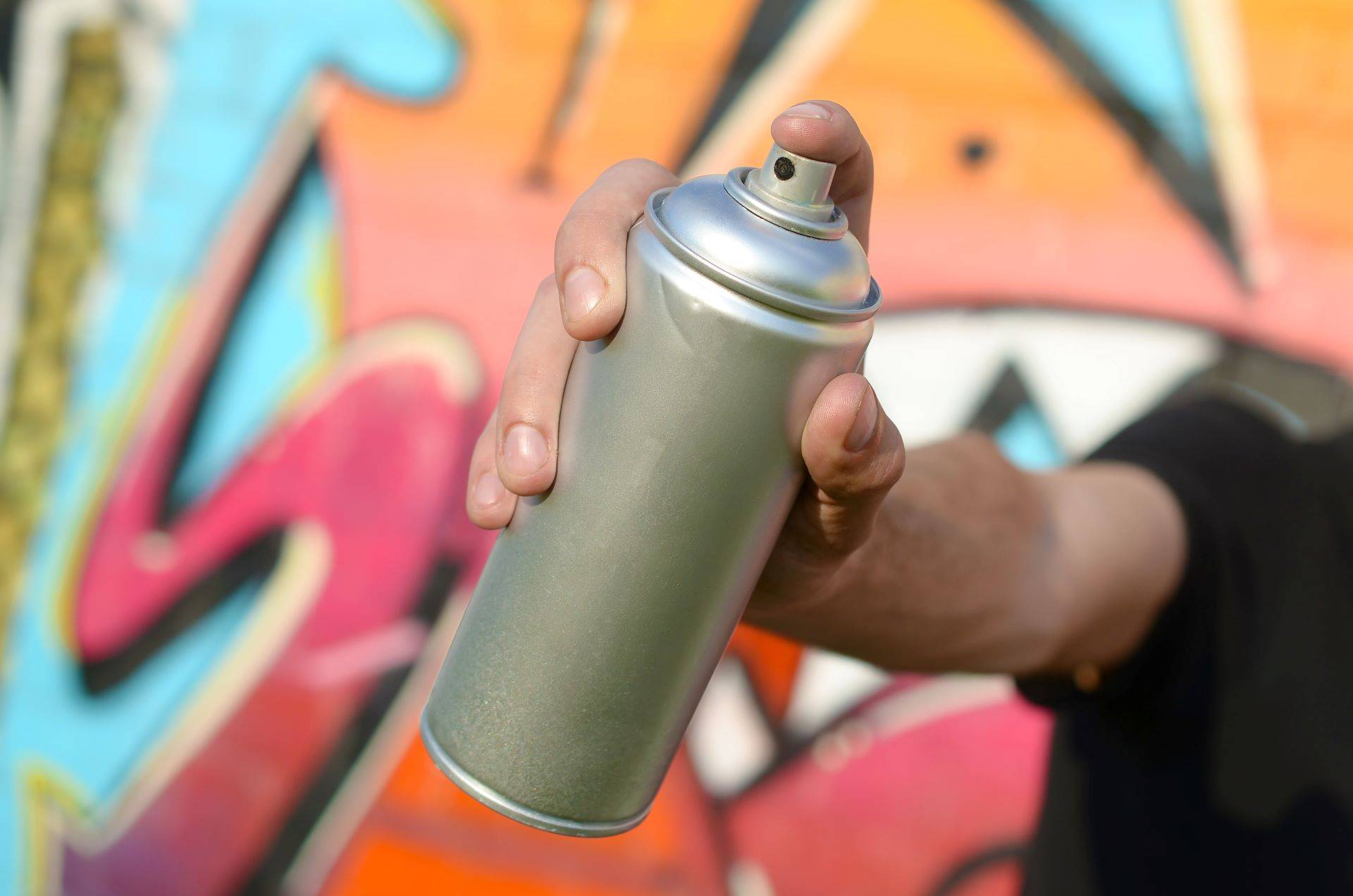 Hand mit Sprühdose vor bunter Graffiti-Wand