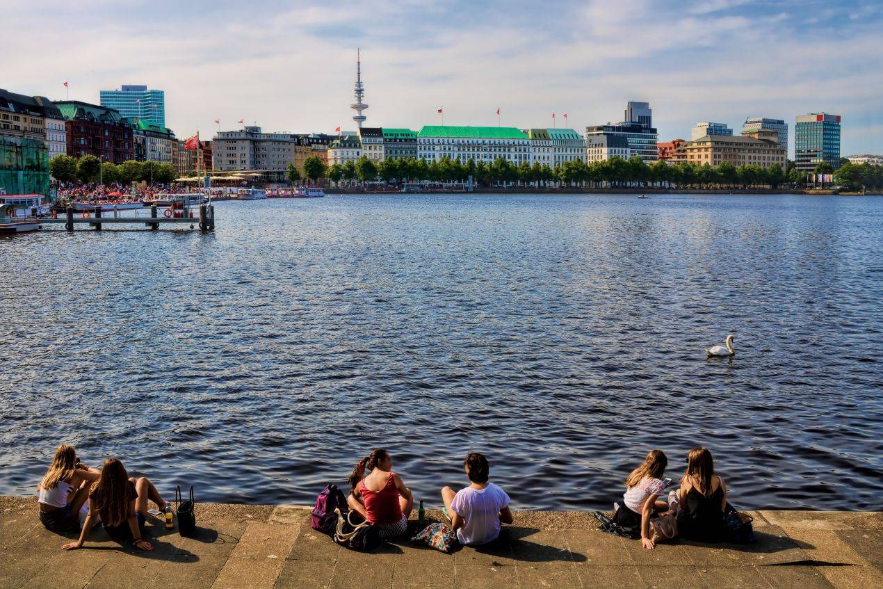 Jugendliche sitzen entspannt an der Binnenalster in Hamburg mit Blick auf die Stadt – entspannter Moment waehrend einer Klassenfahrt Hamburg
