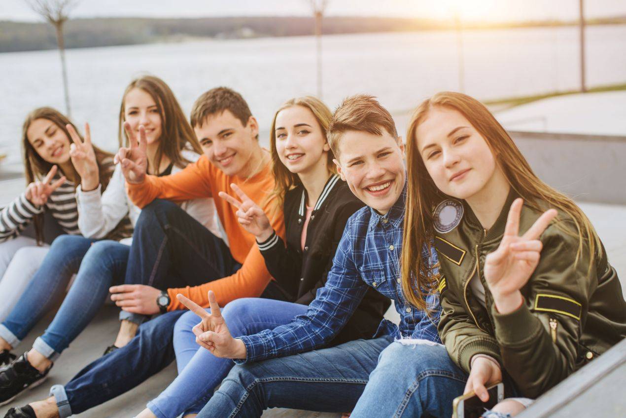 Schuelergruppe sitzt lachend am Wasser bei Sonnenuntergang auf Klassenfahrt in Hamburg