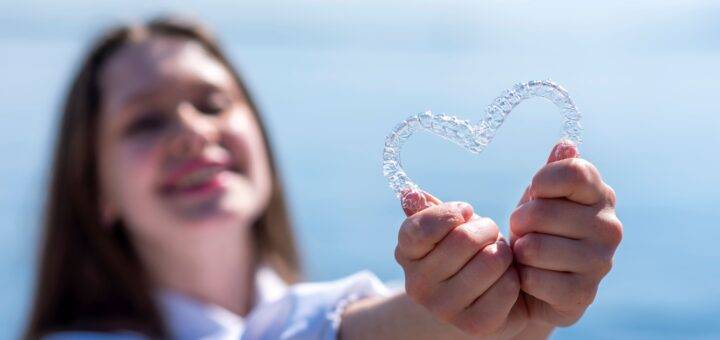Maedchen haelt transparente Zahnschiene in Herzform vor sich – moderne Kieferorthopaedie Essen mit unsichtbarer Zahnspange
