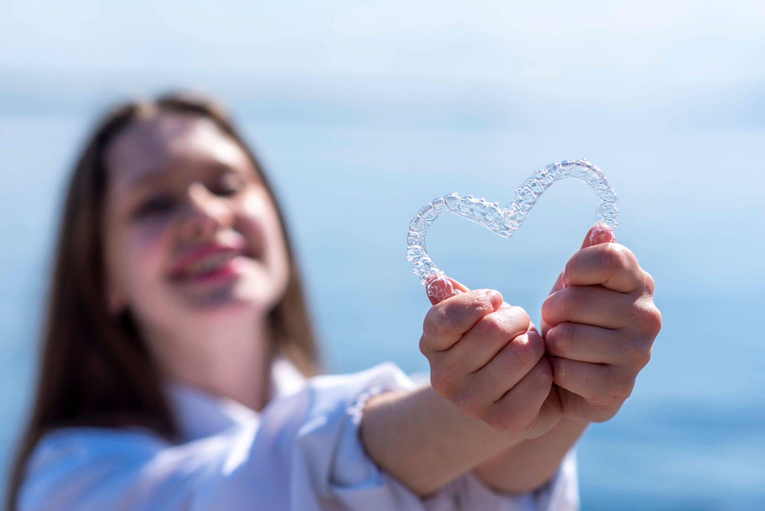 Maedchen haelt transparente Zahnschiene in Herzform vor sich – moderne Kieferorthopaedie Essen mit unsichtbarer Zahnspange